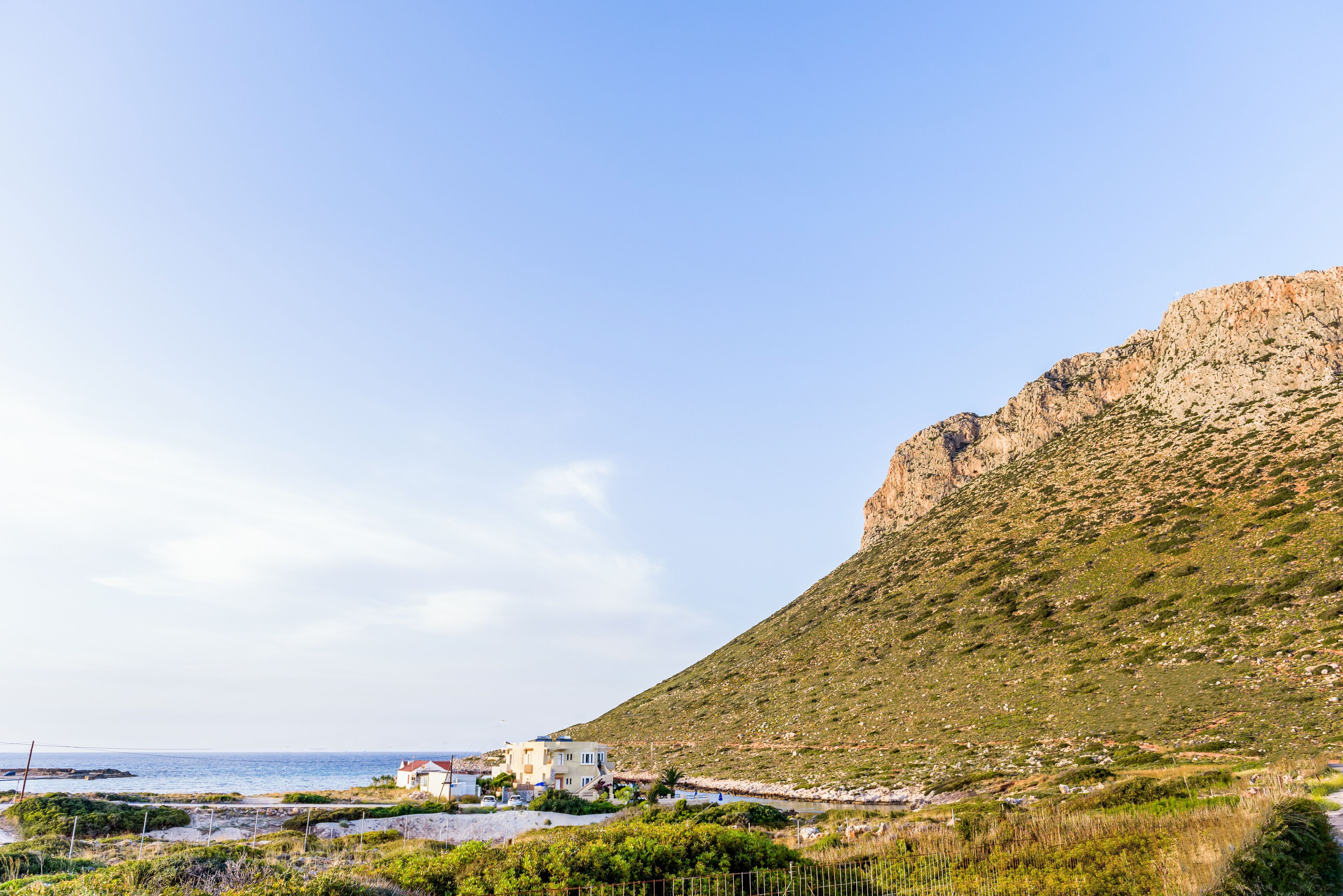 A coastal building with a view of the sea and a hill.
