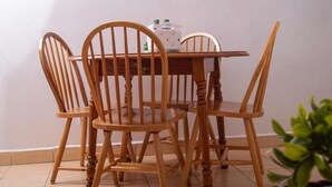 A dining table with four wooden chairs, a white tablecloth, and a small appliance on the table.
