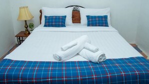 A neatly made bed with white linens, blue plaid bedspread, and two blue plaid pillows.