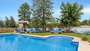 Una piscina con agua azul, rodeada de sillas reclinables azules y una valla de madera.