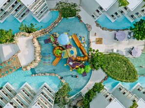 Eine Vogelperspektive eines Resorts mit mehreren Schwimmbecken, einer Wasserrutsche und Liegebereichen.