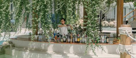 Zona de bar interior con piscina, rodeada de plantas colgantes y un pilar de madera.