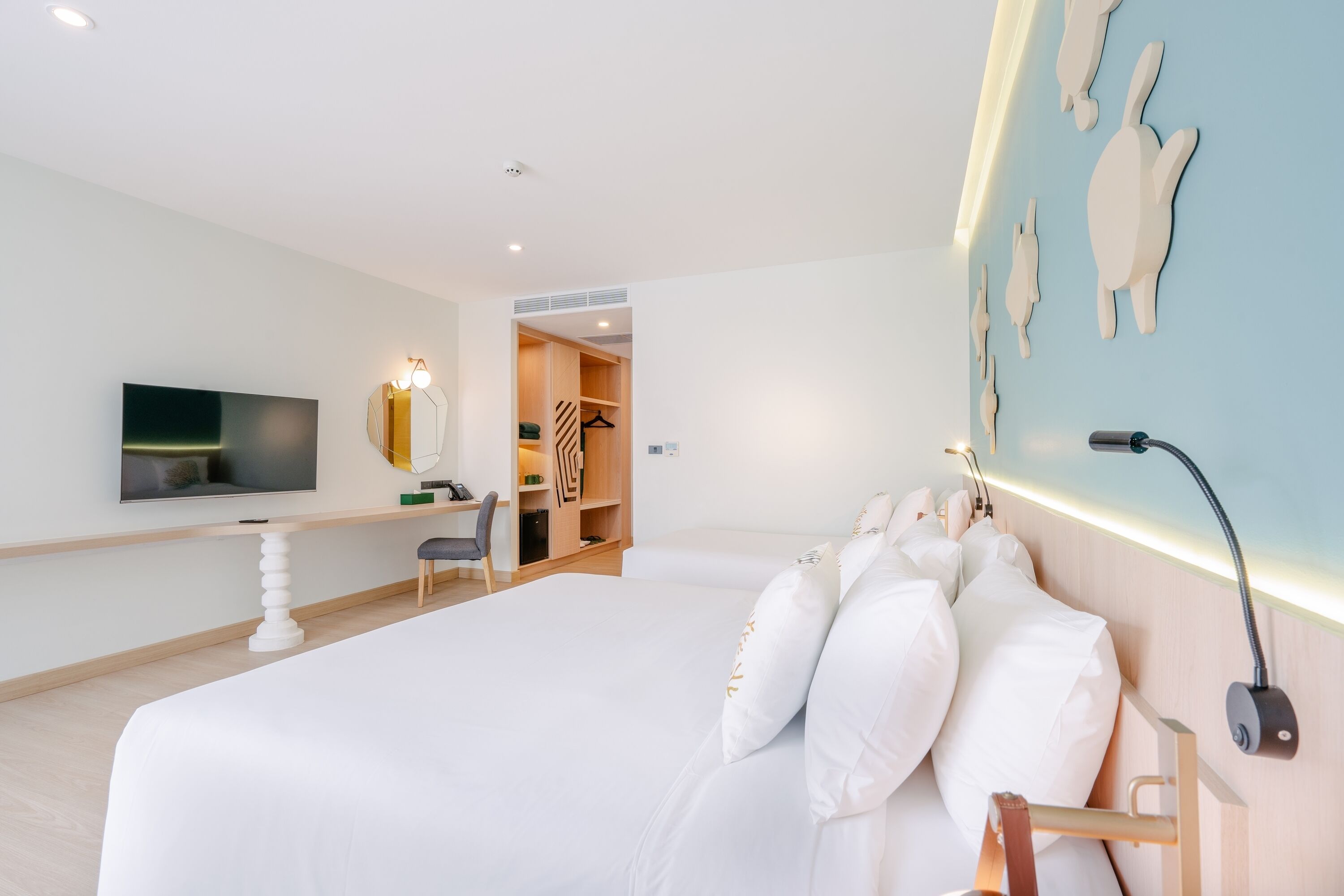 A modern hotel room with a large bed, a TV, a desk, and a walk-in closet.