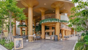 A modern building with a circular design, featuring a central atrium with a staircase, surrounded by outdoor seating areas and greenery. - Phuket Emerald Beach Resort (Karon)