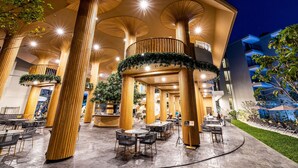A modern outdoor seating area with round tables and chairs, surrounded by tall wooden columns with circular cutouts. - Phuket Emerald Beach Resort (Karon)