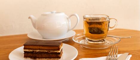 A table with a white teapot, a glass cup with tea, and a slice of cake on a plate.