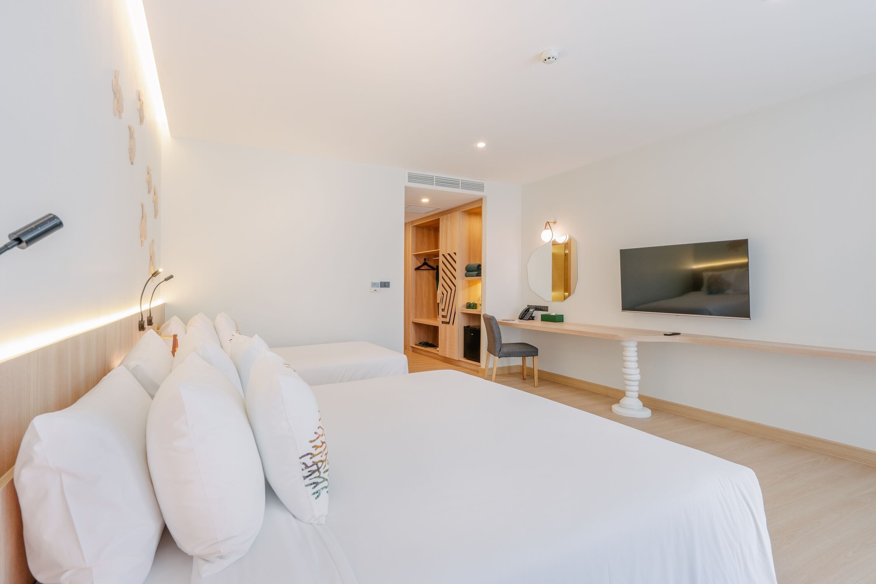A hotel room with a large bed, a desk with a flat-screen TV, a wardrobe, and a mirror.