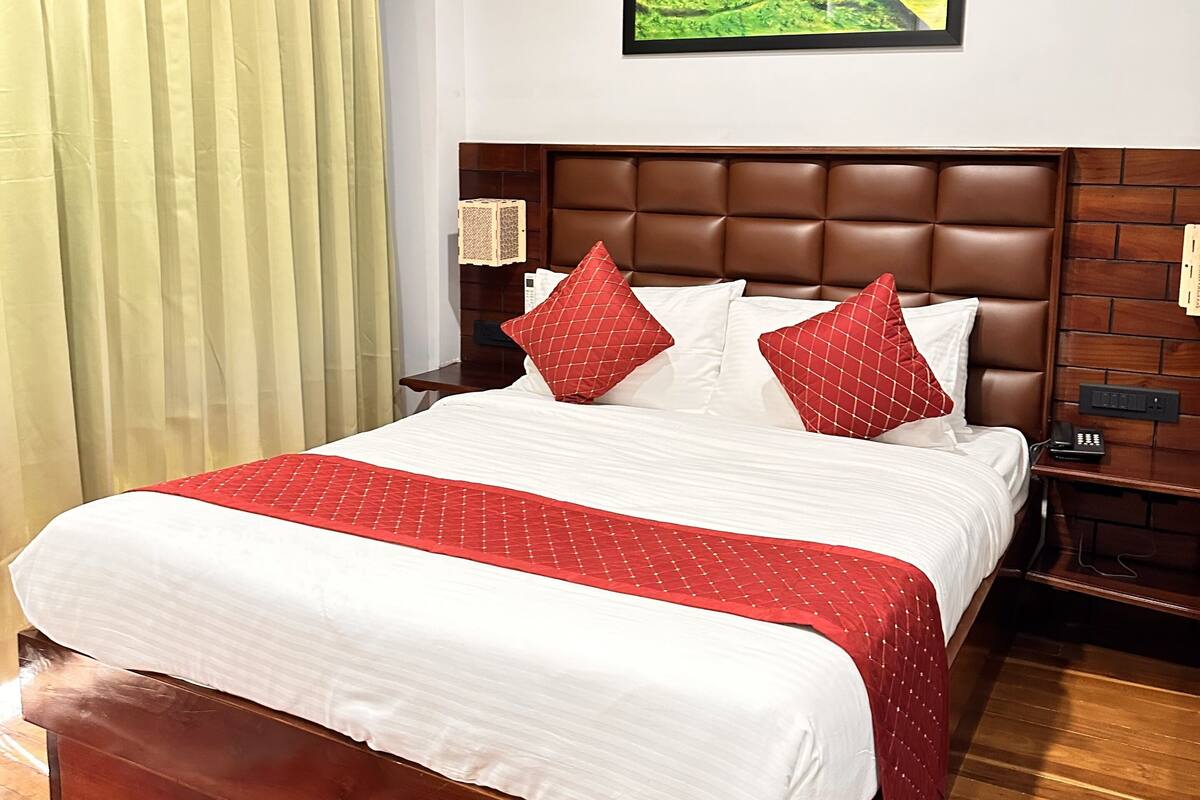 A neatly made bed with a red and white bedspread, a wooden headboard, and a landscape painting above it.