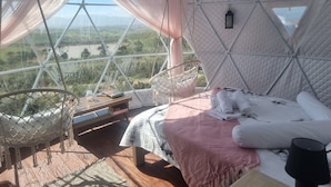 A cozy, well-lit tent with a bed, a hanging chair, and a small table with a book and a glass jar.