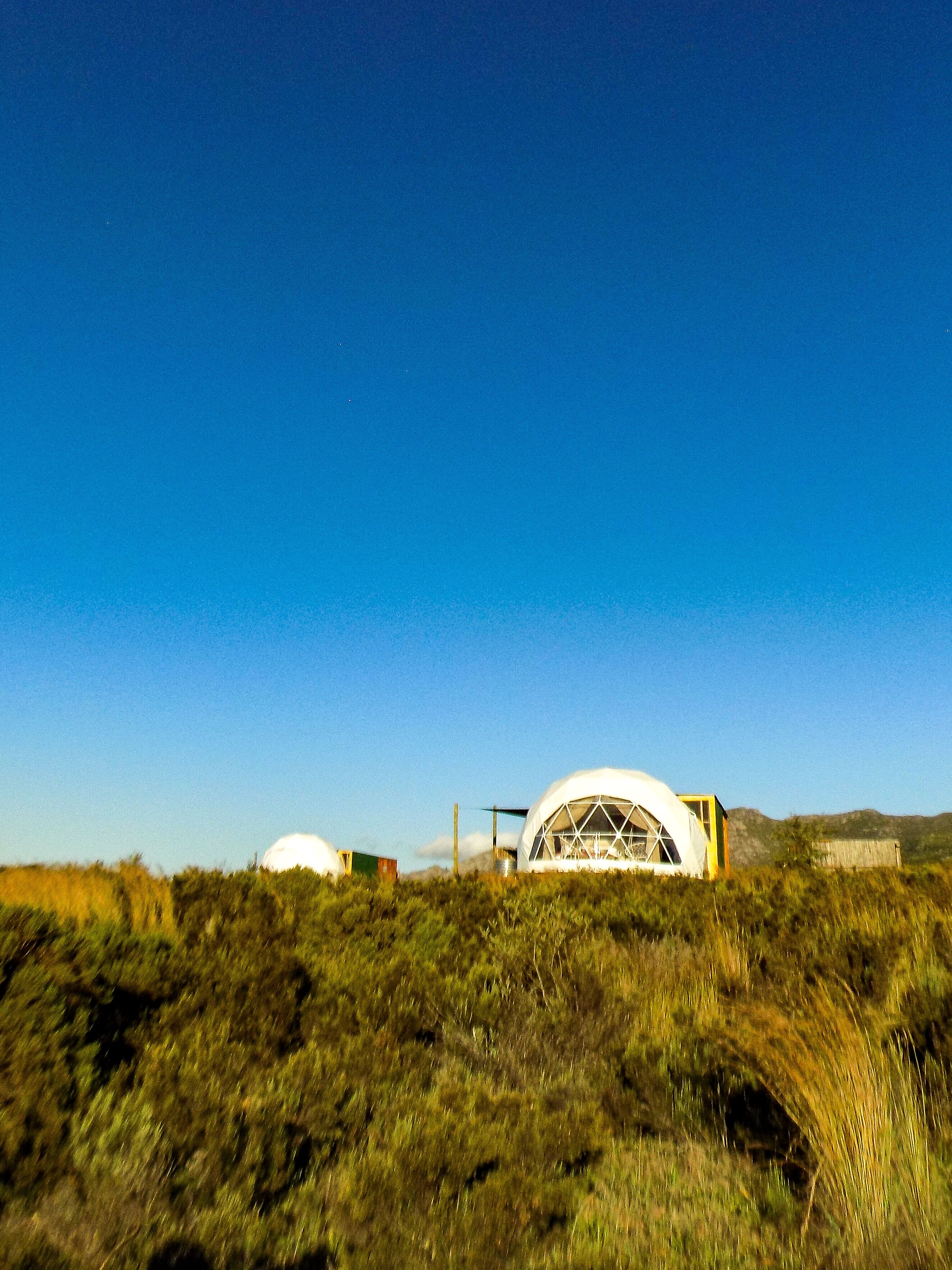 A dome-shaped building with a large central window, surrounded by a grassy landscape and a clear blue sky.