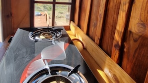 A rustic cabin interior with a wood-paneled wall, a stove, and a window offering a view of a rural landscape.