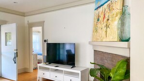 Una sala de estar con un televisor sobre un mueble blanco, una chimenea y un cuadro encima.