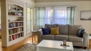 Una sala de estar con sofá, mesa de centro, estantería y ventana con cortinas.