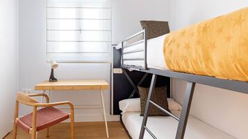 A bunk bed with a yellow patterned blanket, a desk with a lamp, and a chair.