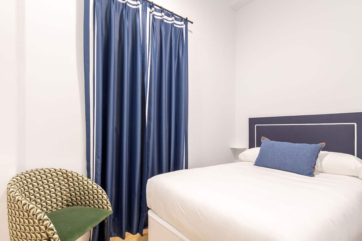 A bedroom with a bed, a headboard, a nightstand, a lamp, and a chair.