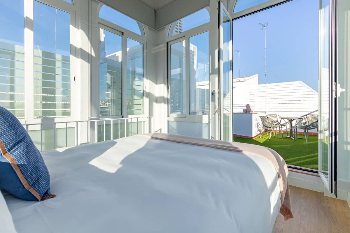 A bedroom with a large bed, a view of a grassy outdoor area, and a balcony with a table and chairs.