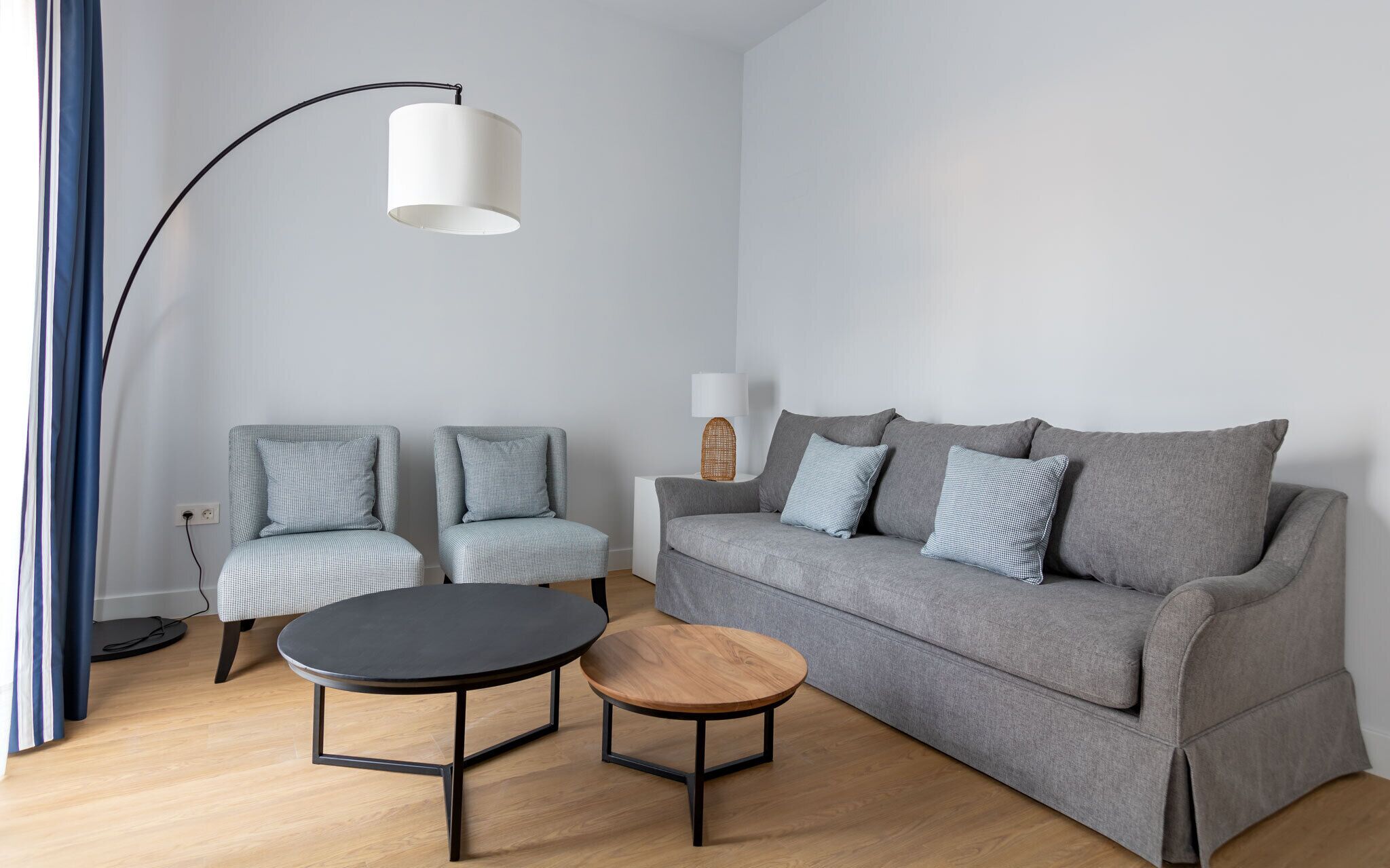A modern living room with a grey sofa, two matching armchairs, a small round wooden table, and a floor lamp.