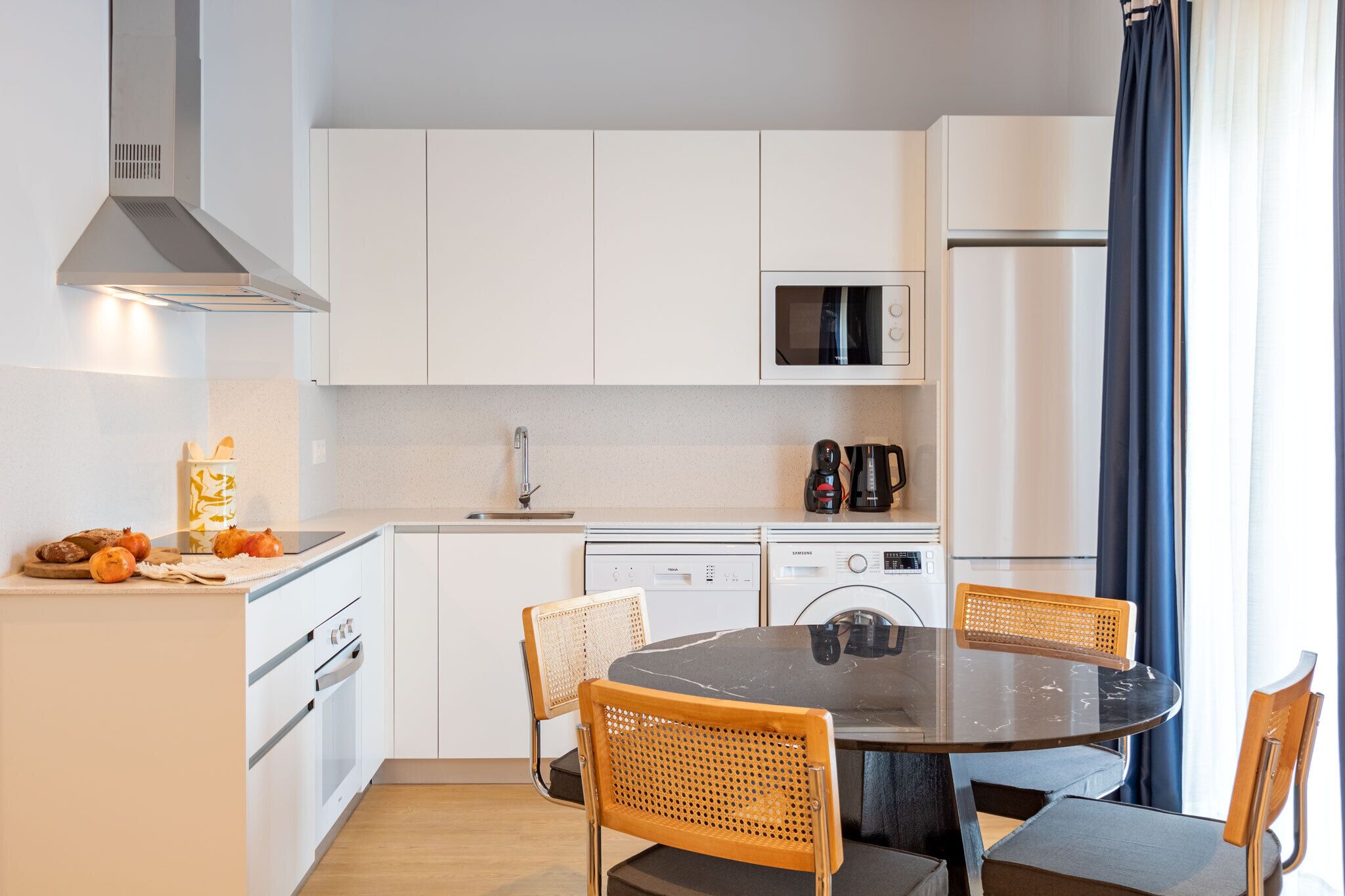 Een moderne keuken met witte kasten, een magnetron, een koffiezetapparaat en een eethoek met een ronde tafel en vier stoelen.