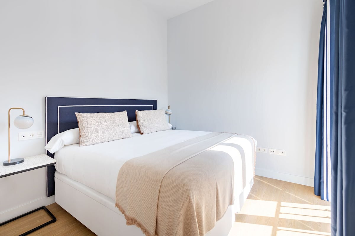 A neatly made bed with a blue headboard, a bedside lamp, and a beige throw blanket.