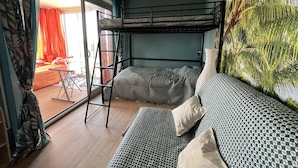 Ett rum med en våningssäng, en stege, en soffa och ett stort fönster med gardiner.
