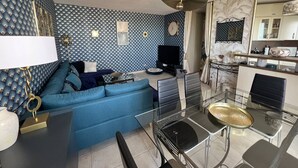 Ett modernt vardagsrum med en blå soffa, ett matbord i glas och en köksdel med skåp och en mikrovågsugn.