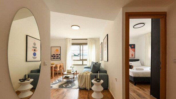 A modern living room with a sofa, coffee table, and a dining area with a table and chairs. - MAMAD - Pet-friendly 2BR Apt & Kitchen (Tel Aviv)