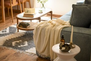Un salon chaleureux avec un canapé, une petite table ronde sur laquelle sont posés des livres, un porte-bougie décoratif et un tapis à motifs.