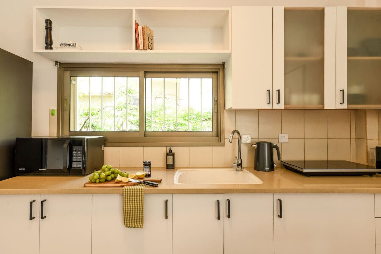 A modern kitchen with white cabinets, a microwave, a sink, and a window with a view of greenery.