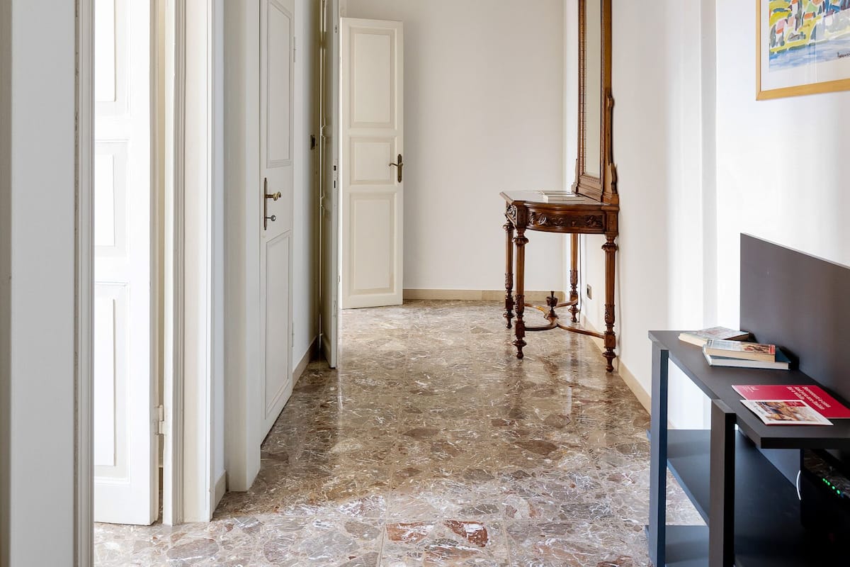 Un couloir doté d’un sol en marbre, de portes blanches, d’une chaise en bois et d’un tableau encadré accroché au mur.