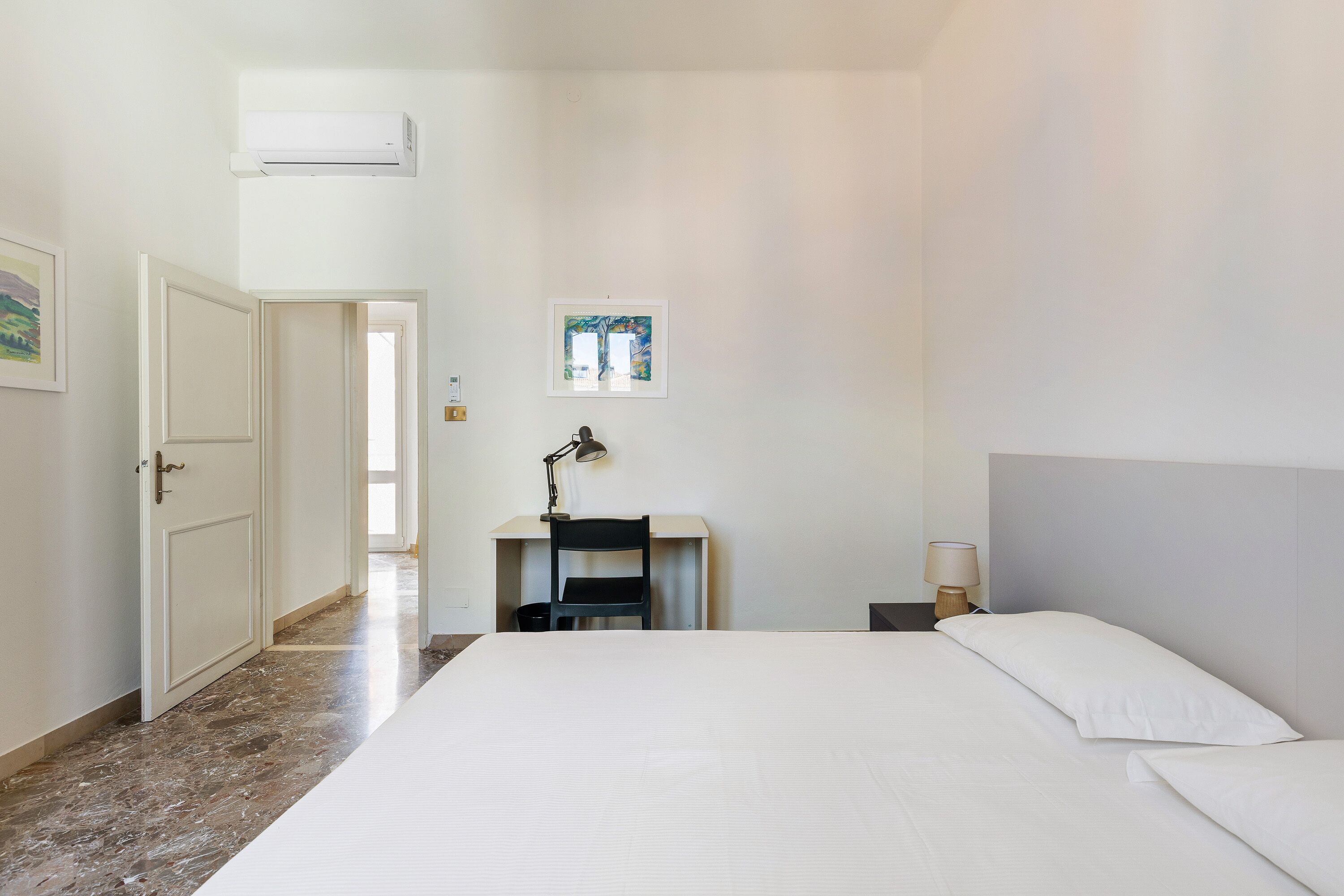 Un dormitorio con una cama, un escritorio con silla, una lámpara y un cuadro en la pared.