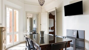 A dining area with a glass-top table, wooden chairs, a chandelier, and a flat-screen TV mounted on the wall. - Irnerio Apartments by Wonderful Italy (Bologna)