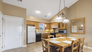 A kitchen with wooden cabinets, a dining table with chairs, a refrigerator, a microwave, and a hanging light fixture. - Peaceful Views, Jetted Tub, Relaxing Fireplace - Condo at StoneBridge (Reeds Spring)