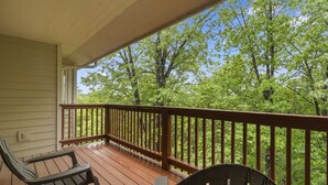 A wooden deck with two chairs and a railing overlooking a lush green forest.