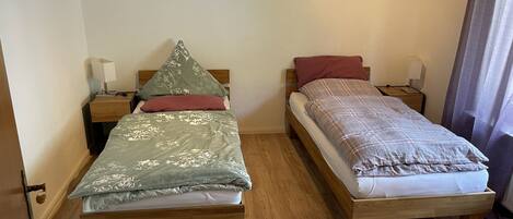 A room with two wooden beds, each with a nightstand and a lamp.