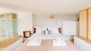 A hotel room with a bed, a nightstand, a wooden wardrobe, a radiator, and a window with blinds. - Lydia Apartment (Stavros)