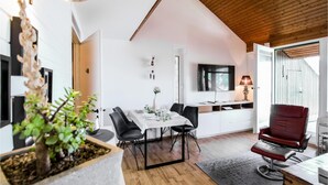 Een moderne eetruimte met een houten plafond, een eettafel gedekt met witte tafelkleden, zwarte stoelen en een rode barstoel.