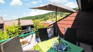 Een balkon met een tafel gedekt voor twee personen, een rieten stoel en uitzicht op een dorp.