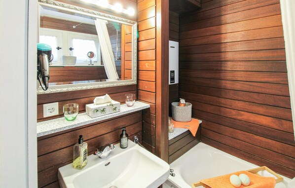 Een badkamer met houten lambrisering, een wastafel, een spiegel, een handdoekhouder en een douchehoek.