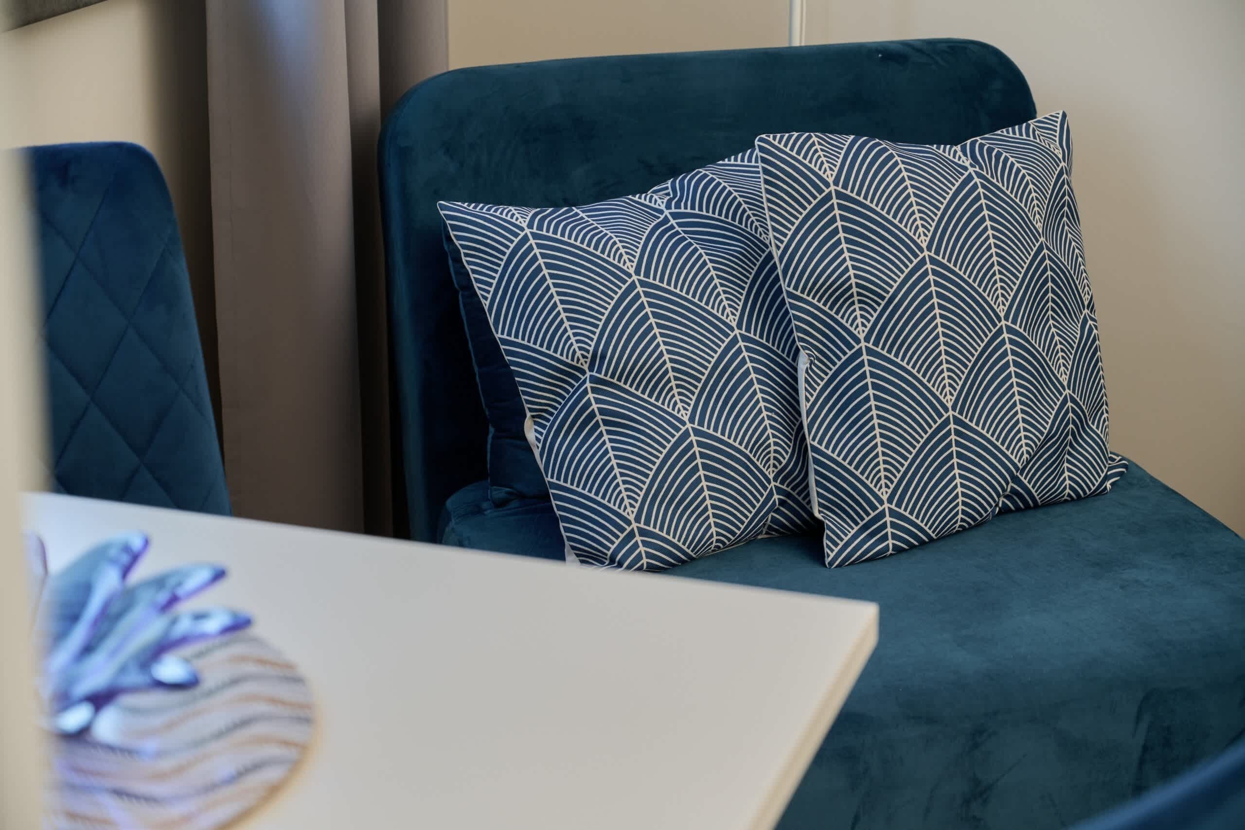 A room with a dark green sofa, patterned pillows, and a quilted blanket.
