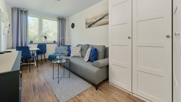 A modern living room with a sofa, chairs, a dining table, and a large window. - Compact Studio | Close to Park, Pet Friendly (Wroclaw)