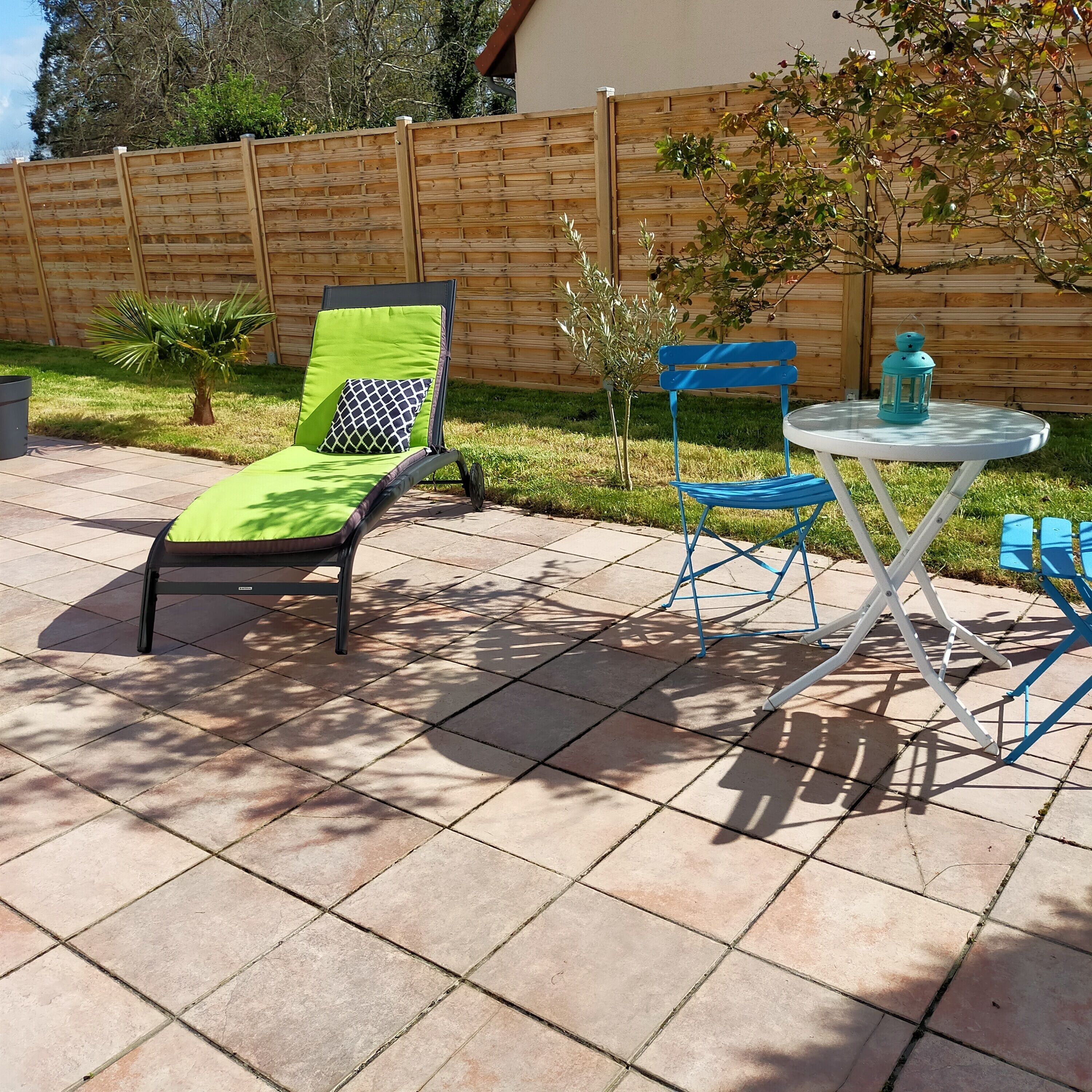 A patio with a lounge chair, a small table, and a blue folding chair.