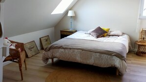 Un dormitorio con techo inclinado, una cama con ropa de cama estampada, un tapete redondo, una silla de mimbre y una mesita de noche con lámpara.