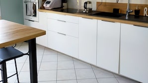 Una cocina moderna con armarios blancos, encimera de madera, horno integrado, microondas, hervidor y un lavabo con grifo.