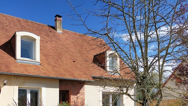 Una casa de dos pisos con techo de tejas rojas, una chimenea de ladrillo y un balcón pequeño.
