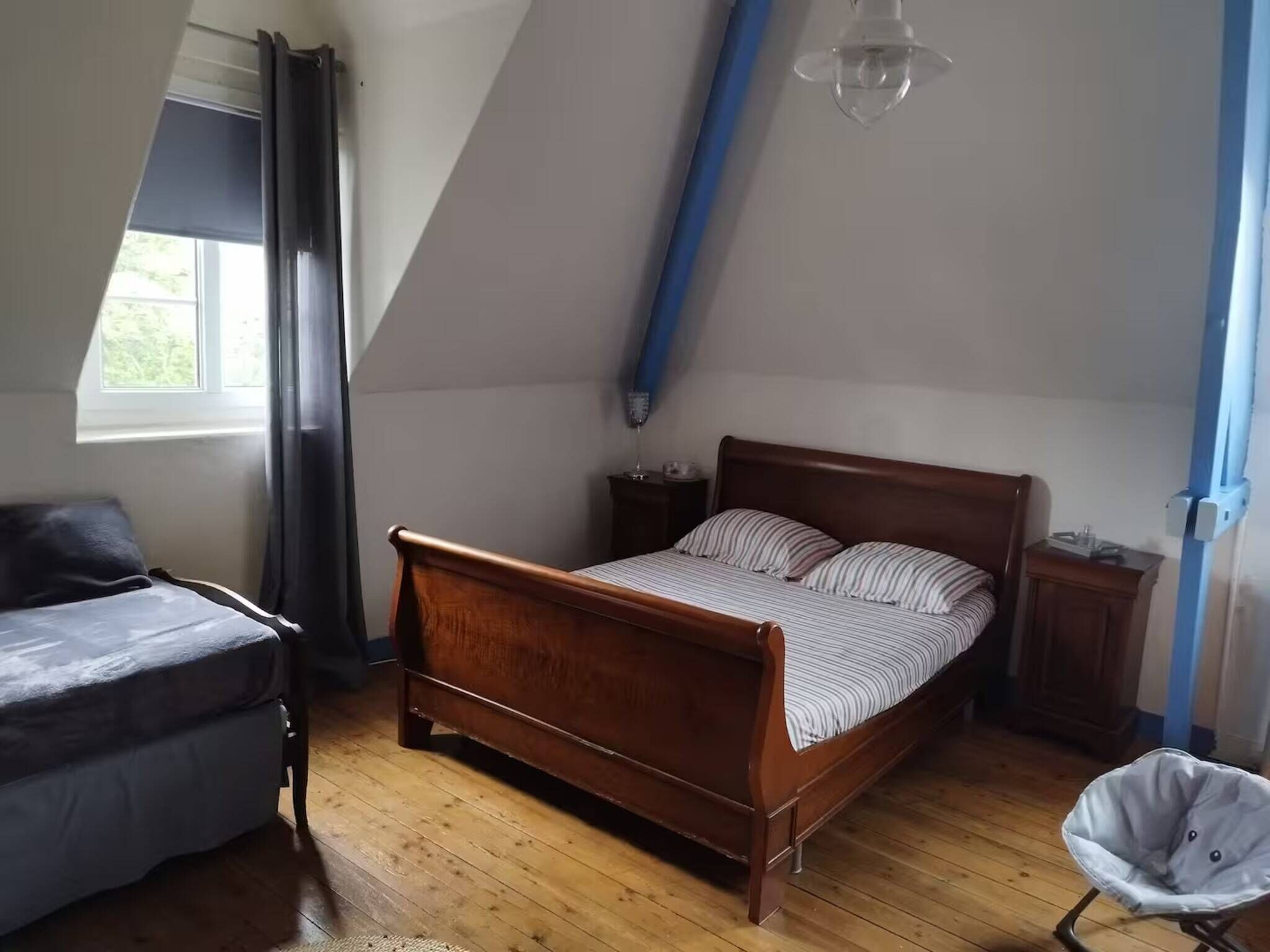 Un dormitorio con una cama de madera, una silla, una mesita y una lámpara colgante.