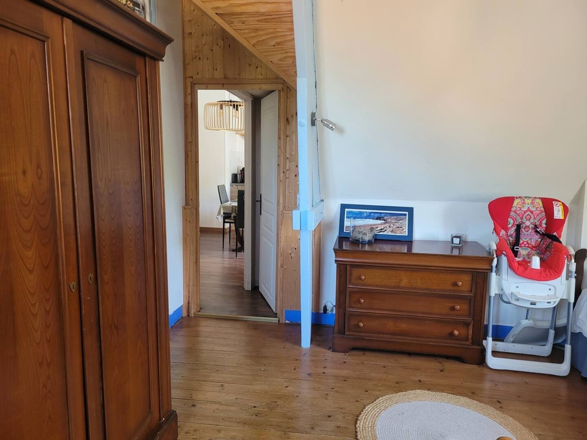A hallway with wooden flooring, a wooden cabinet, a dresser, and a baby stroller.