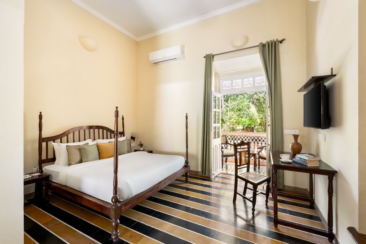 Ein Schlafzimmer mit einem Himmelbett, einem Fernseher, einem kleinen Tisch mit Büchern und Blick auf einen Balkon mit Gartenmöbeln.
