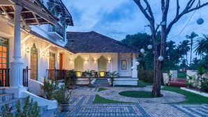 A two-story house with a tiled roof, a covered porch, and a paved courtyard with a circular pattern. - Silva Heritage Resort Goa (Colva)