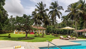 A swimming pool with lounge chairs and a palm tree-lined garden. - Silva Heritage Resort Goa (Colva)