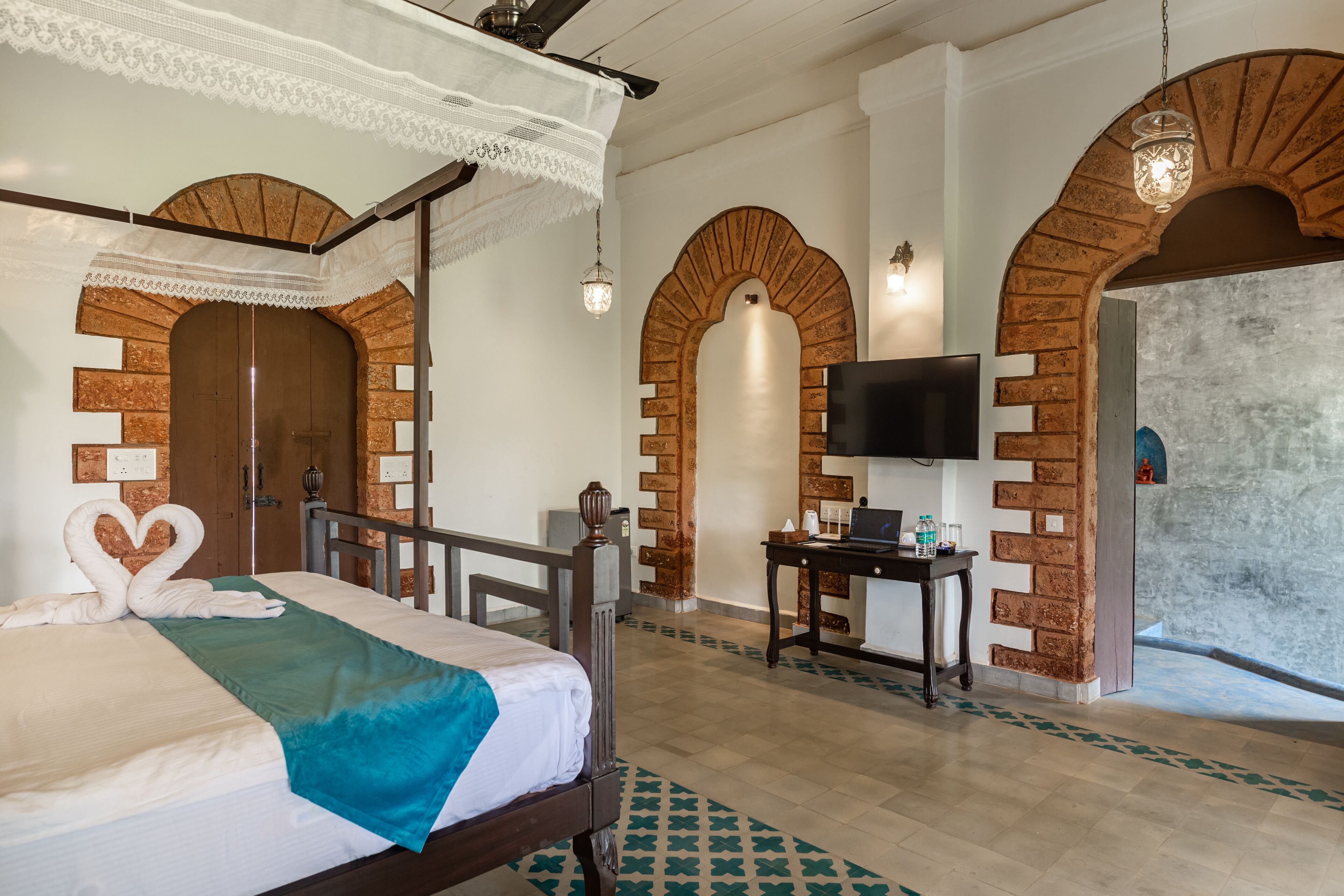 Una habitación de hotel con cama, escritorio, televisor y arcos decorativos.